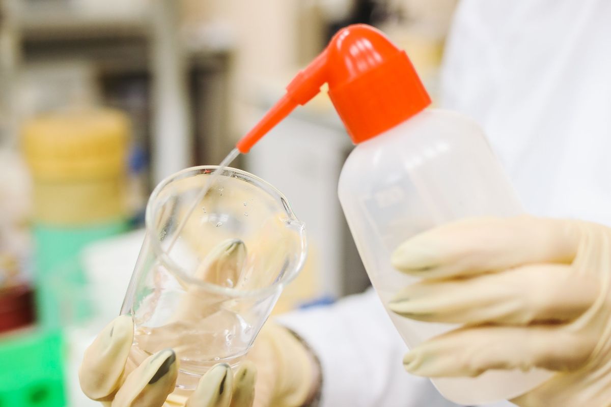 Lab technician filling a beaker with a wash bottle for cosmetic formulation