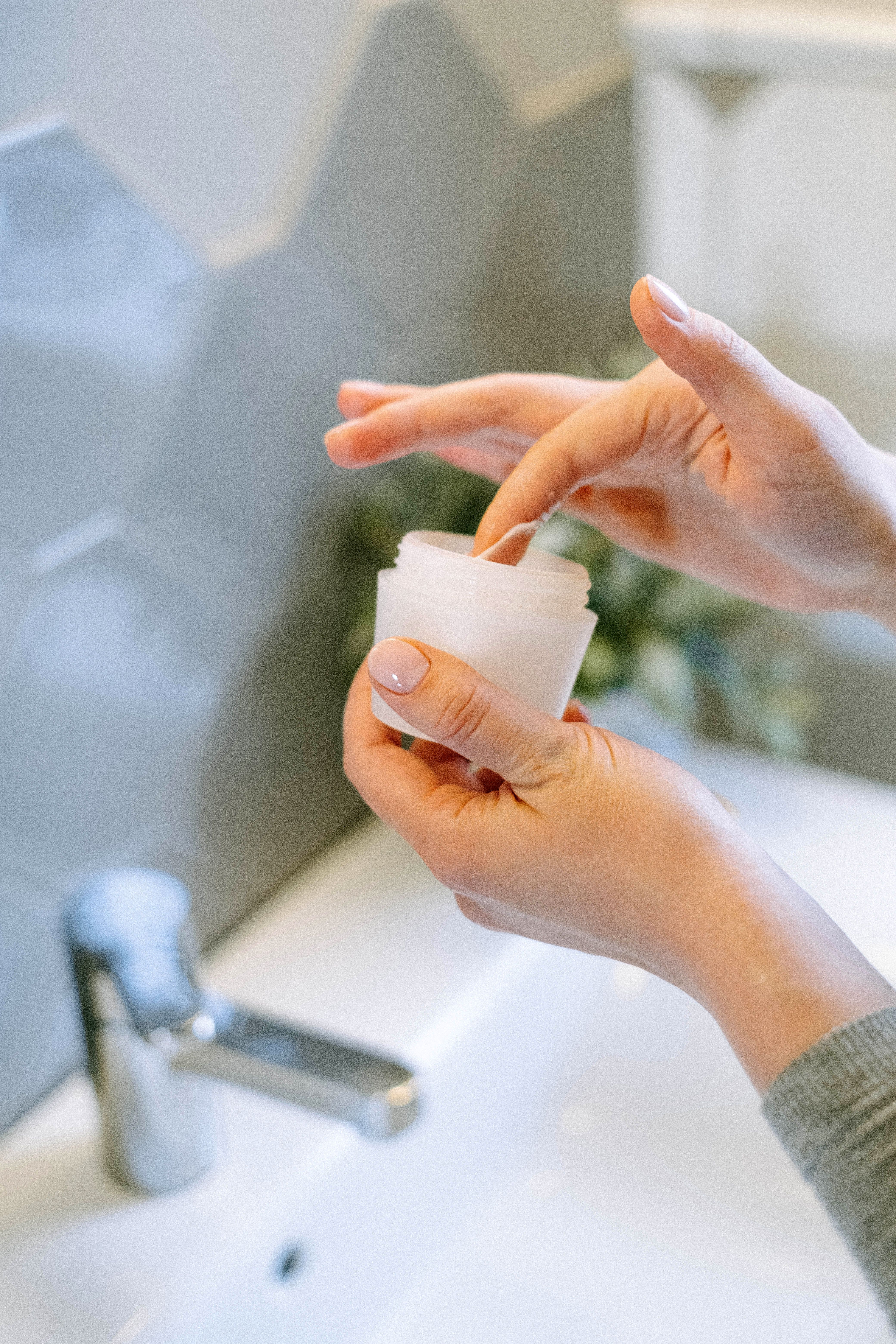 Hands dipping into a jar of finished cream cosmetic manufacturing